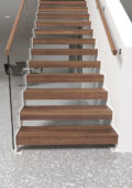 Profil en ståltrappa med glasräcke och överliggare i trä
